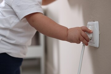Child safety at home. Little boy taking plug out of power outlet indoors, closeup