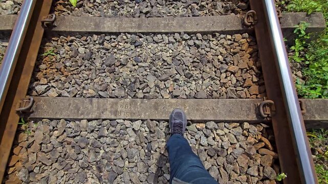 POV of a person walking fast along a rural railway track, with only the legs visible in frame. Sense of movement and journey through a quiet countryside setting, with railway sleepers and tracks.