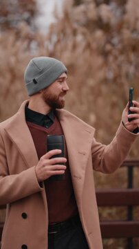 Smiling Man Capturing a Moment with His Smartphone and Coffee Mug in a Park