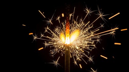 Close-up macro shot of a bright sparkler emitting a dense shower of golden sparks against a black background, symbolizing celebration and joy.