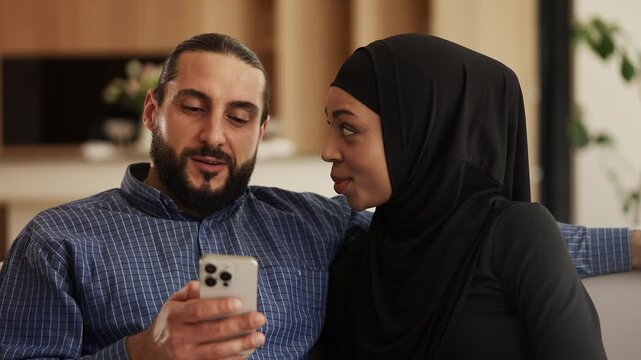 Cheerful Arab couple choosing luxury house on cellphone, online property search