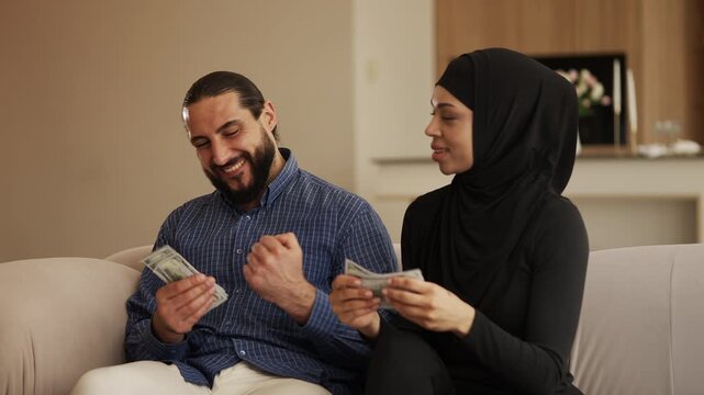 Positive Muslim couple counting money at home, satisfied with high income
