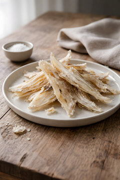 Ultra-realistic food photo of traditional Icelandic dried fish (hardfiskur) on a minimalist ceramic plate. Rustic Nordic wooden table, soft natural daylight, clean Scandinavian aesthetic.