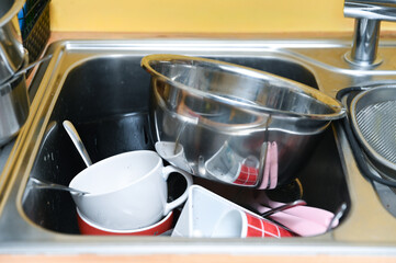 Dirty dishes in a stainless steel kitchen sink under a modern faucet. Daily household chores, messy kitchens, cleaning routines, home life, and a realistic concept of home lifestyle.