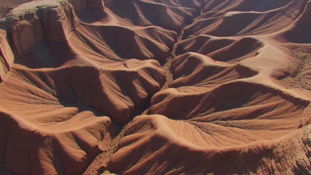 Aerial drone view over rugged red clay canyon formations in the Utah desert, showcasing deep erosion textures and arid badlands geology.