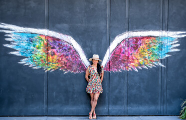A woman stands in front of a colorful wing mural © ExploringandLiving