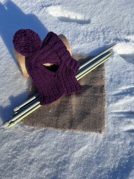 Winter knitting: purple wool mittens and yarn on snow with knitting needles