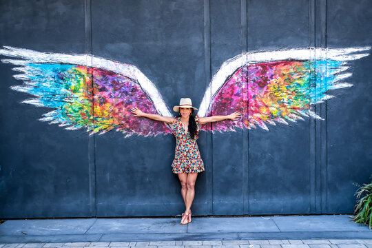 A woman stands in front of a colorful wing mural, posing for the camera