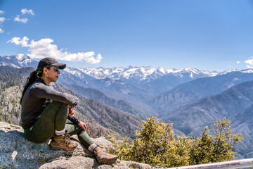 Fototapeta premium A woman is sitting on a rock overlooking a mountain range