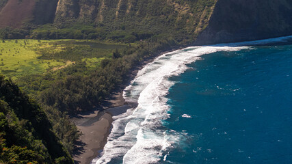Aerial view of Waipi'o Black Sand Beach landscape and coastal cliffs and ocean waves on Big Island...
