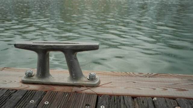 A close-up view of a metal dock cleat affixed to a wooden pier over calm water.