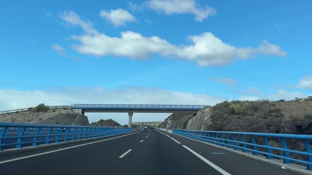 Road trip driving POV, empty highway through rocky mountain cut, bridge ahead, blue sky clouds, travel video background, transportation, journey concept.