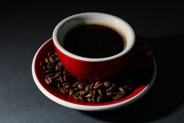 Obraz premium Cup of aromatic coffee and beans on black background, closeup