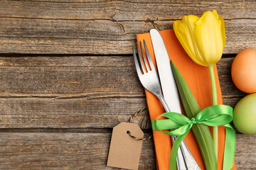 Easter table setting. Beautiful silverware with tulip and painted eggs on wooden background, top...