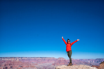 A woman in a red jacket is standing on a mountain top, smiling