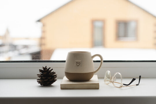 Cozy windowsill with cup, glasses, and pine cone