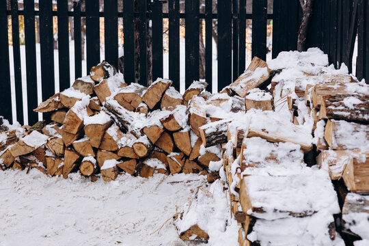 Pile of firewood covered in snow by a wooden fence