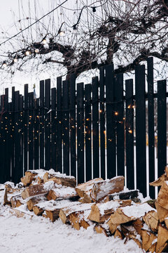 Wintery wooden logs by a black fence with festive lights