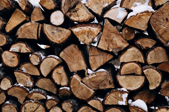 Stacked wooden logs with remnants of snow