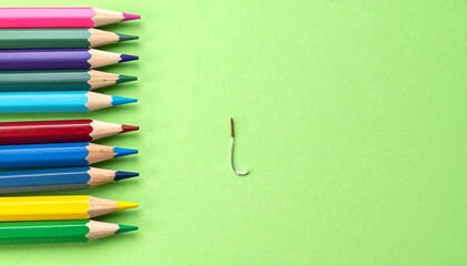 Colorful pencils and a paper clip on a green background, creative concept.