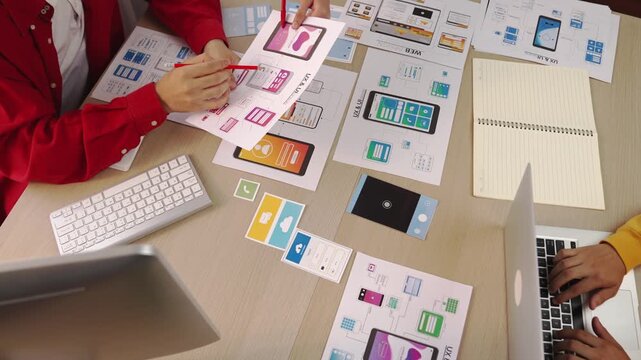 Hand focus of startup company employee present user interface prototype for mobile application to smart co-worker in office workspace. UX UI designer praise function of icon design on paper. Synergic