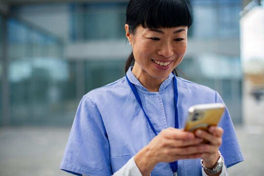 Smiling healthcare worker using smartphone outside hospital
