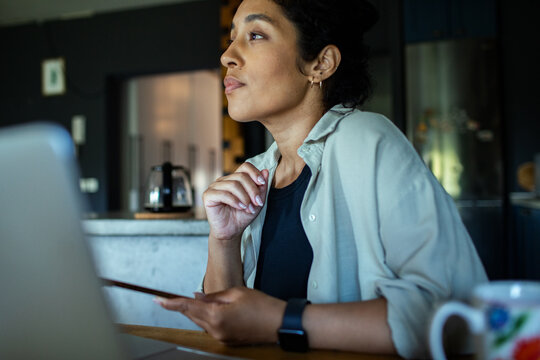 Thoughtful young woman using smartphone while working in home kitchen