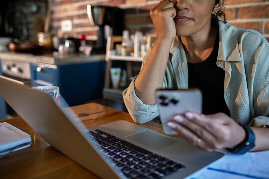 Woman using smartphone and laptop in home kitchen