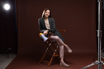 Fototapeta premium Professional film director with megaphone on chair against brown background