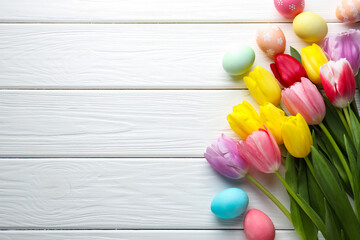 Painted Easter eggs and beautiful tulips on white wooden table, flat lay. Space for text