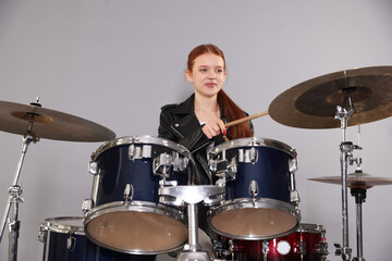 Teenage girl with drumsticks and drums on light grey background