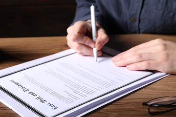 Woman signing Last Will and Testament at wooden table, closeup