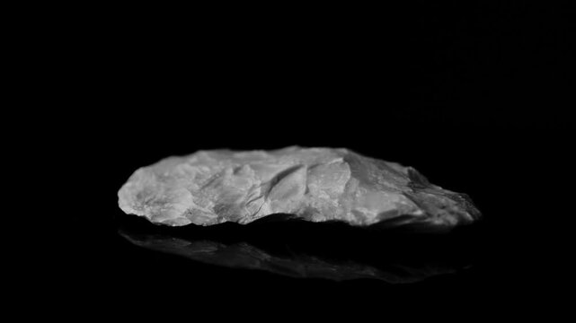 Paleolithic knife. Biface technology. Man manipulates the prehistoric tool, flint flaking from core flakes. History of technological evolution. 4K slow motion. black and white
