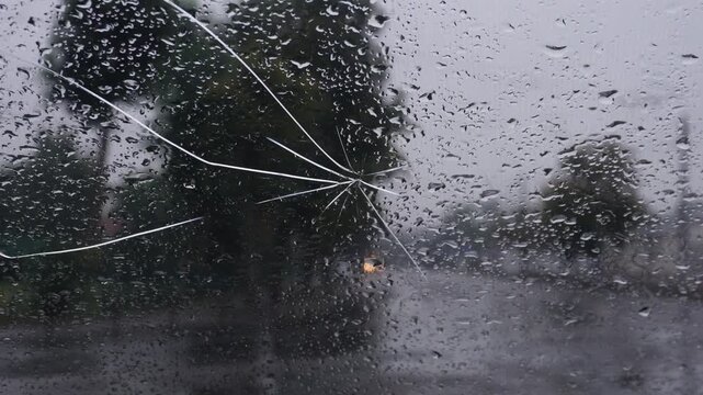 Rain splashes on a broken car window while driving down a wet street in a city during a stormy day