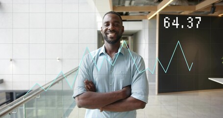 Smiling man in blue shirt standing arms crossed in office atrium, glass railing and chart 64