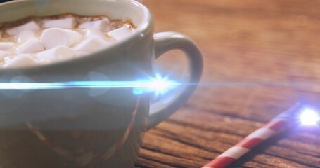 Resting ceramic mug with cocoa and mini marshmallows on wood table, striped straw, lens flare