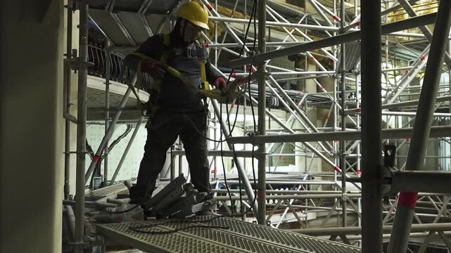 Worker securing construction materials at scaffolded job site.
