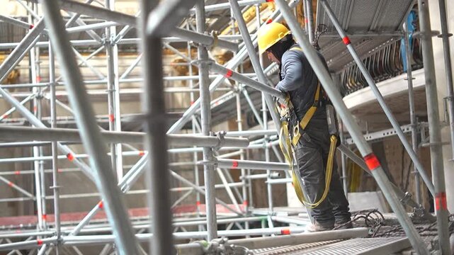 Equipped construction worker wearing safety harness on metal scaffolding.