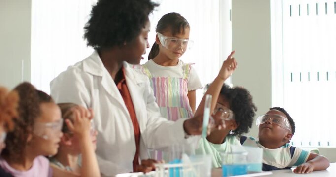 African American teacher lifting test tube showing blue liquid at bench as children raising hands