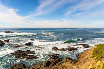 Rocky ocean coastline with waves under blue sky at Half Moon Bay, California