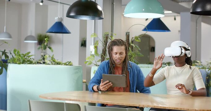 African American pair testing white VR headset woman lifting hand as man guiding tablet at table