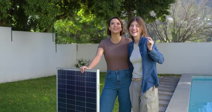Diverse women by pool holding solar panel while right woman pointing, planning placement for sun