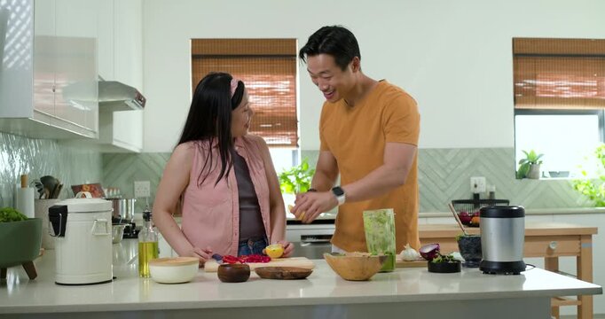 Diverse couple prepping meal at home kitchen island, man leaning guiding hands then muddling lemon