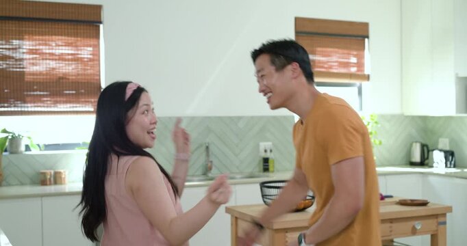 Diverse couple dancing at bright kitchen island after woman lifting arm, man mirroring for fun
