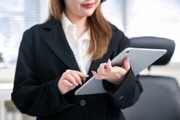 An Asian businesswoman is using a tablet at her desk in an office.