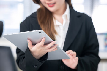 An Asian businesswoman is using a tablet at her desk in an office.