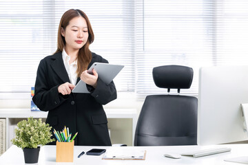 An Asian businesswoman is using a tablet at her desk in an office.