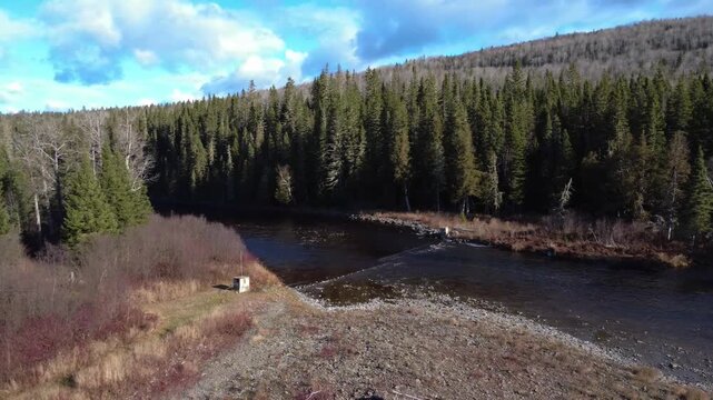 The remains of Atlantic salmon counting and observation facilities on the Matapedia River flowing through an autumnal forest. Quebec, Canada, 2025.