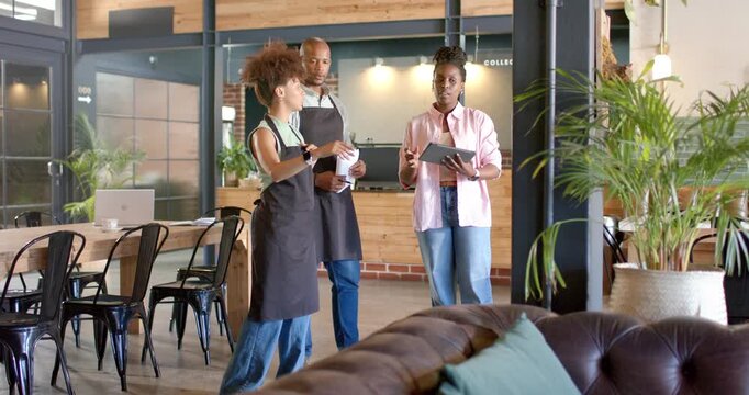 African American cafe team planning left gesturing right pointing tablet or papers two black-aproned