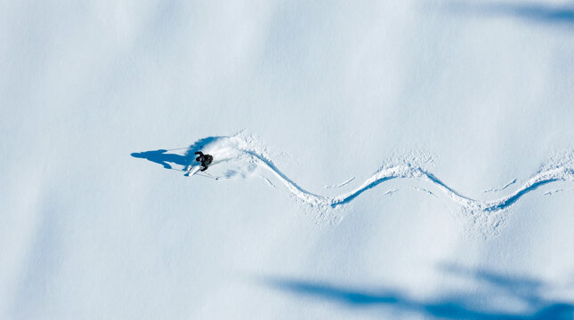 Aerial view of a lone skier carving a sinuous path through fresh powder snow